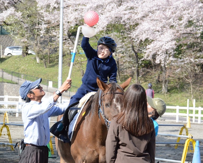 「RDA横浜」の野口陽さん(左)の指導で、馬上でボールを使い体を伸ばす吉村渉さん=横浜市神奈川区で