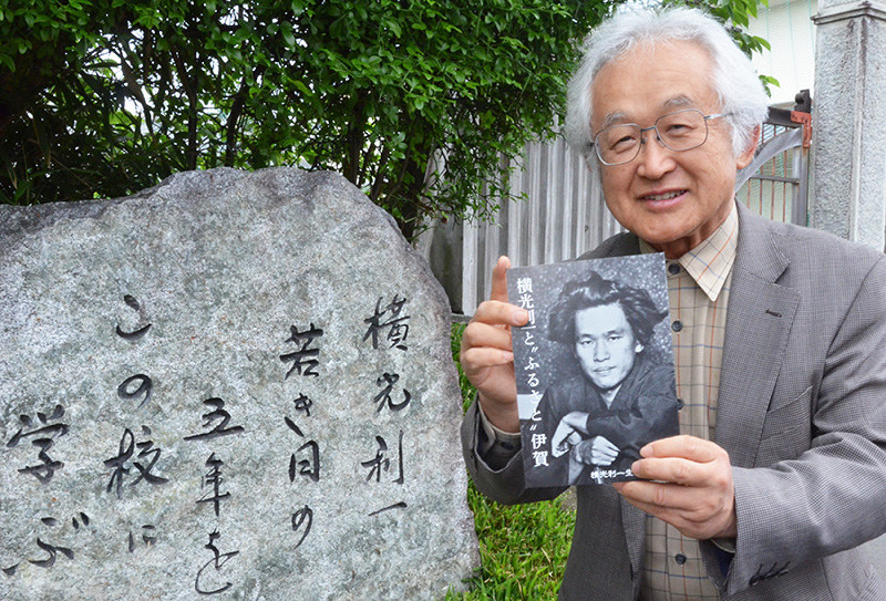 岸宏子さんがきごうした石碑の横で、刊行した本を持つ福田和幸さん=三重県伊賀市の上野高校前で、大西康裕撮影
