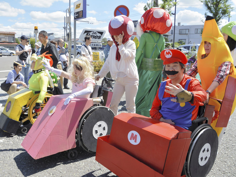 車椅子ごとに、ゲームのキャラクターに扮し、沿道に手を振る参加者ら=神奈川県鎌倉市大船で