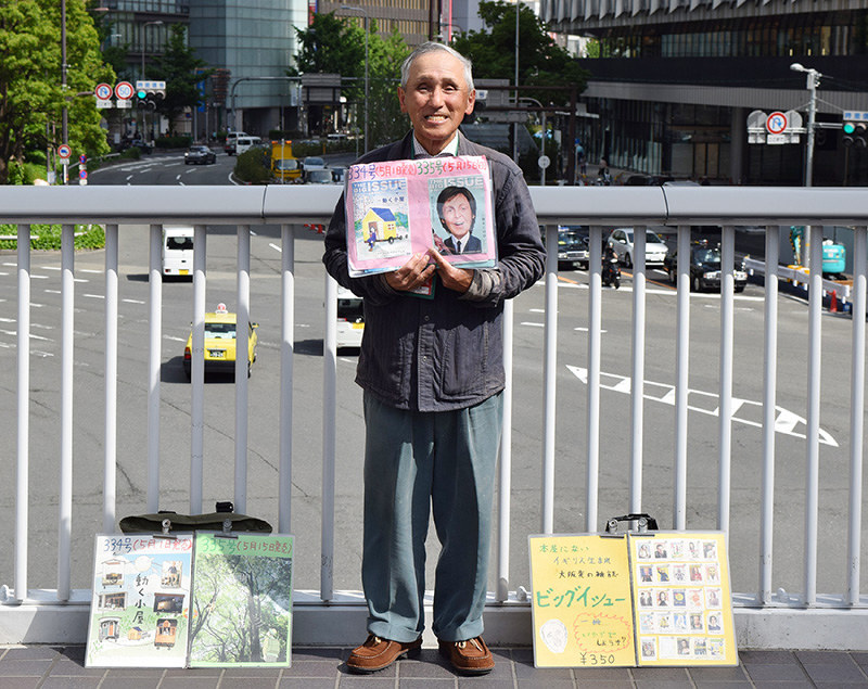 JR大阪駅近くの歩道橋でビッグイシューを販売する濱田進さん。看板は手作り=大阪市北区梅田の阪急百貨店前の歩道橋で、谷田朋美撮影