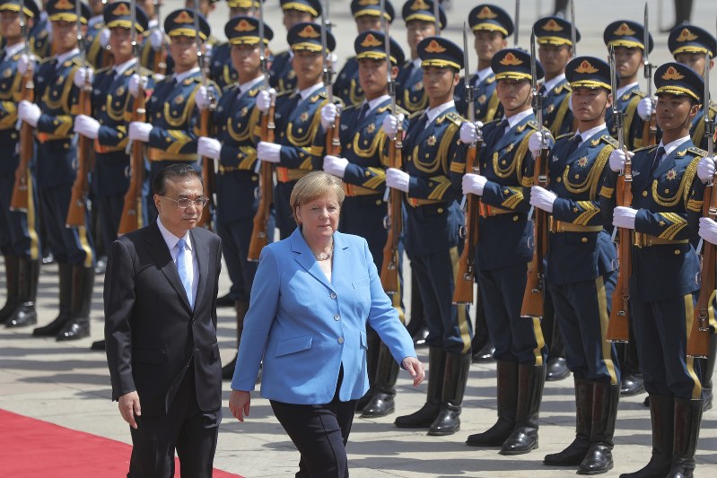 歓迎式典で並んで歩くドイツのメルケル首相(右)と中国の李克強首相=北京の人民大会堂で2018年5月24日、AP