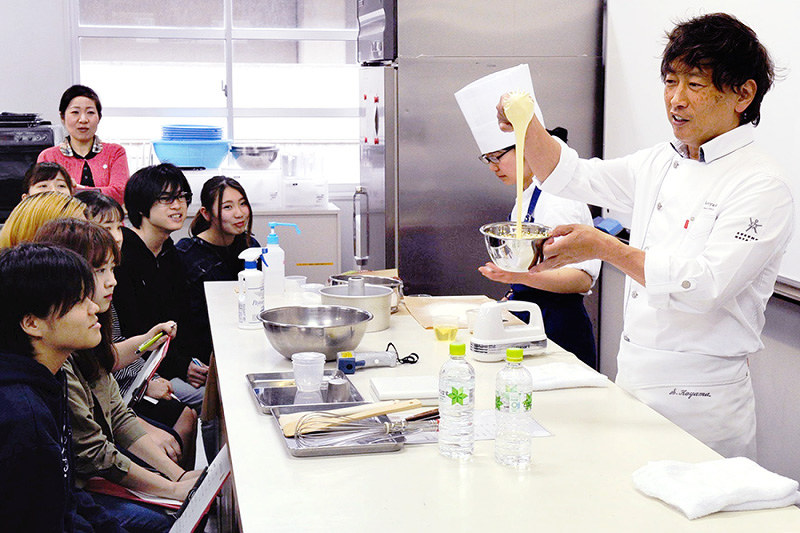 シフォンケーキ作りの実演をしながら生徒に話しかける小山進さん=神戸市長田区池田谷町2の長田商高で、峰本浩二撮影