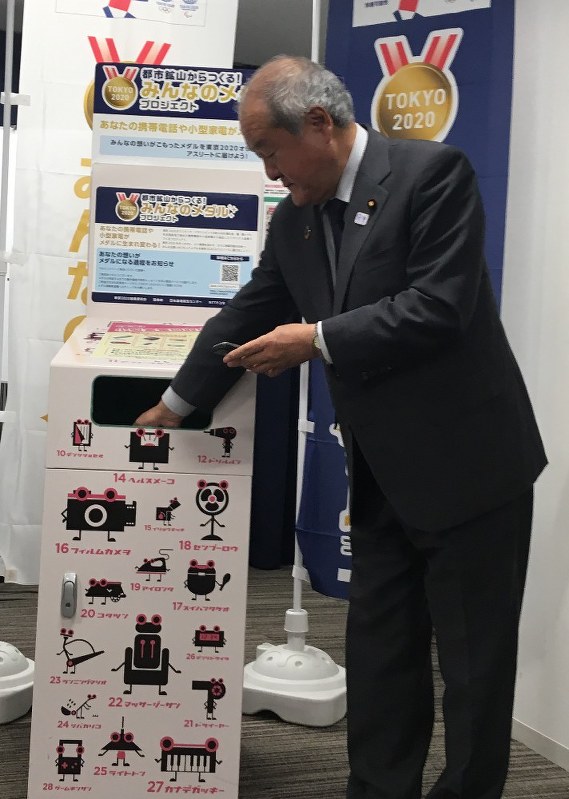 東京五輪・パラリンピックのメダルの材料として回収ボックスに使用済み携帯電話を投入する鈴木五輪担当相=内閣府で2018年6月15日午前8時55分、円谷美晶撮影