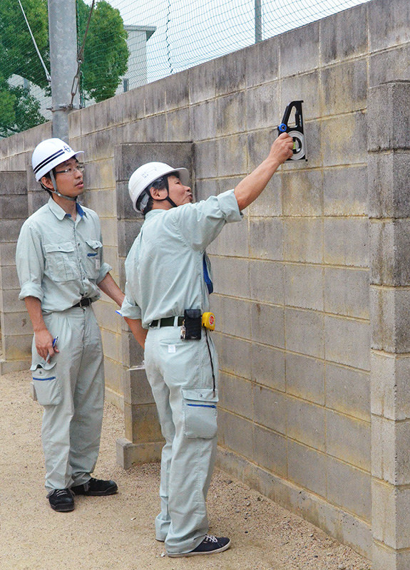 水準器でブロック塀に傾きがないか調べる滋賀県草津市教委の担当者=同市野路町の市立老上小で、礒野健一撮影
