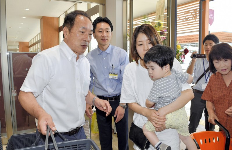 スーパー「ブイチェーンネモト」で買い物客を出迎える根本茂樹さん(左)=福島県楢葉町北田の「ここなら笑店街」で2018年6月26日、乾達撮影