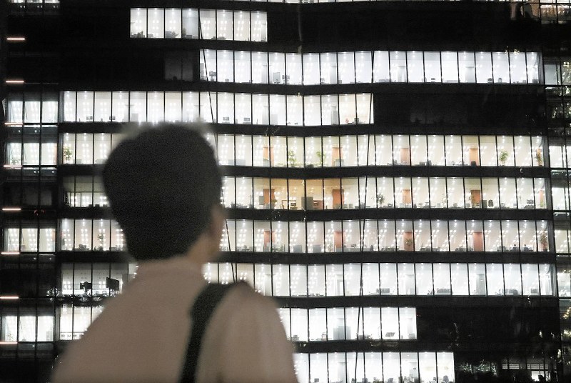 「責任があるから、みんな黙々と残業するんですよね」。システムエンジニアの男性は、明かりのともるオフィスを見上げた=東京都千代田区で2018年6月27日午後8時37分、玉城達郎撮影