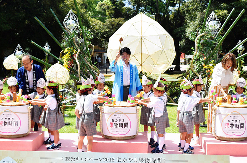 「おかやま果物時間」のオープニングイベントで「桃開き」する伊原木隆太岡山県知事(中央)ら=岡山市北区後楽園で、林田奈々撮影