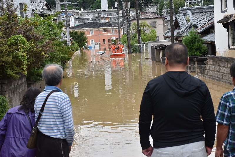 Local residents anxiously look on as rescue workers help other residents evacuate on a boat in Saka Hiroshima Prefecture