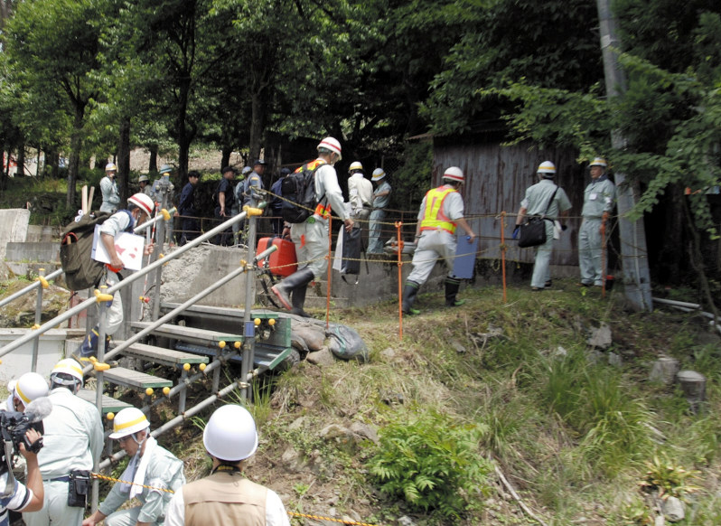 行政代執行の対象となった住宅(右奥)で暮らす男性に退去するよう説得するため調査に入る担当者ら=岩手県釜石市で2018年7月10日、中尾卓英撮影