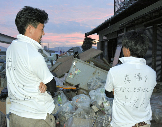 「真備をなんとかせんとおえん」と書かれたTシャツを着てボランティアをする田村純也さん(左)=岡山県倉敷市真備町川辺で2018年7月12日午後7時30分、信田真由美撮影