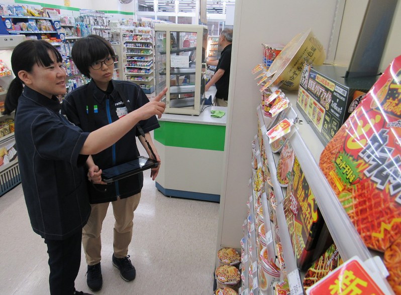 商品の陳列などを店のスタッフと確認する吉田明子さん(左)。笑顔を絶やさない姿が印象的だ=千葉県市川市のファミリーマート妙典駅西口店で