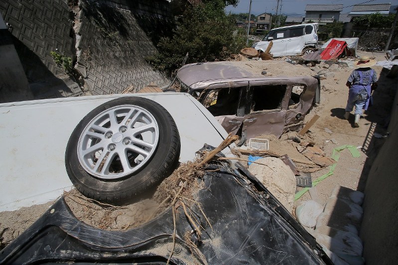 西日本豪雨で車庫に流れ込んだがれきの撤去作業をやめ、自宅に戻る女性。周囲は流された車や土砂が手つかずのまま残る=広島市安芸区で2018年7月24日午前11時26分、和田大典撮影