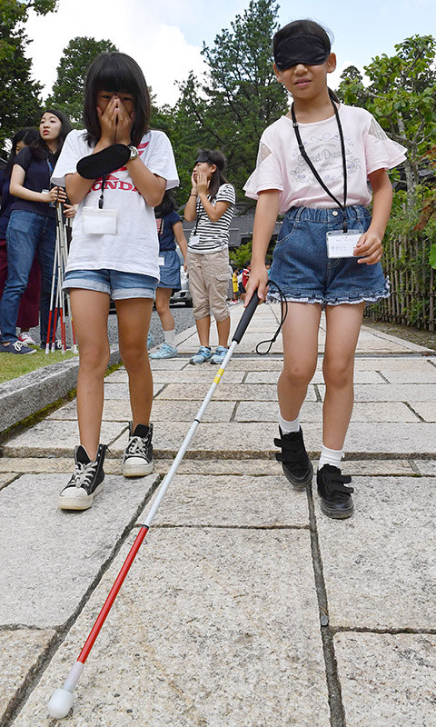 こども高野山夏季大学の体験学習で、アイマスクをつけて白杖を頼りに歩く子供たち=和歌山県高野町で、望月亮一撮影