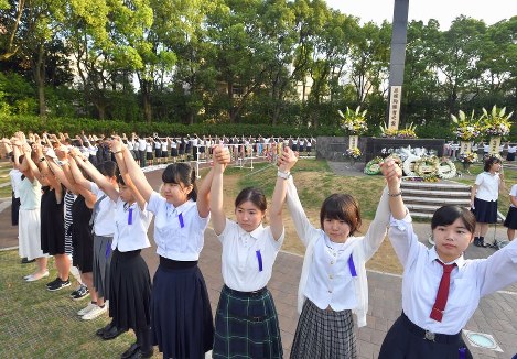 輪になって手をつないで「人間の鎖」をつくる高校生ら＝長崎市の爆心地公園で２０１８年８月９日午前６時５１分、森園道子撮影