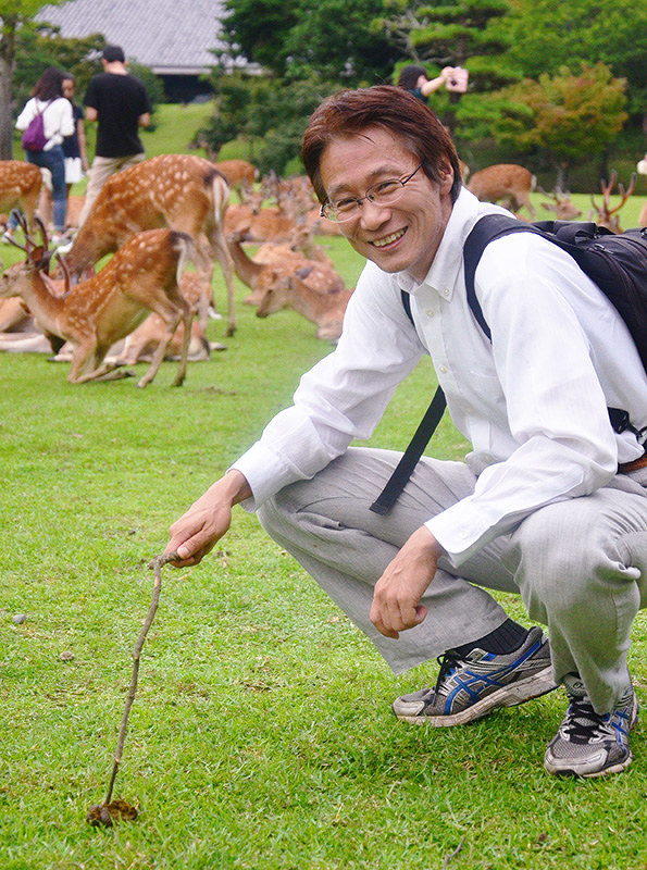 奈良公園で小枝を手に糞虫を探す中村圭一さん=奈良市で、中津成美撮影