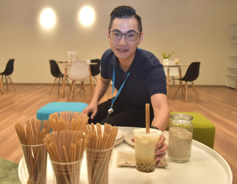 サトウキビのストローをさしたタピオカミルクティーを手にする「鉅田友善材料」の黄千鐘代表。右側の瓶の中にあるのはサトウキビから作ったストローの材料=台湾中部・南投で2018年8月7日、福岡静哉撮影