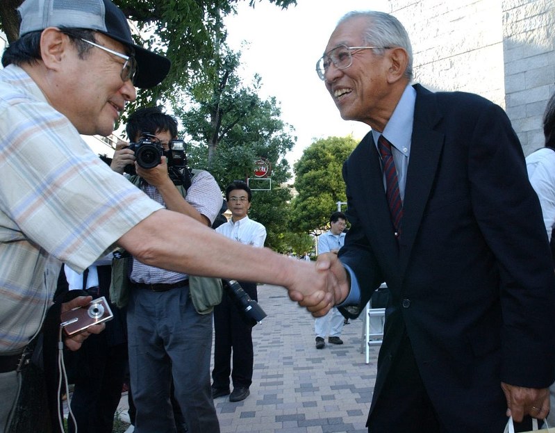 違憲判決を勝ち取り、最高裁前で関係者と笑顔で握手する原告団長の高瀬隼彦さん(右)=最高裁前で2005年9月14日、小出洋平撮影