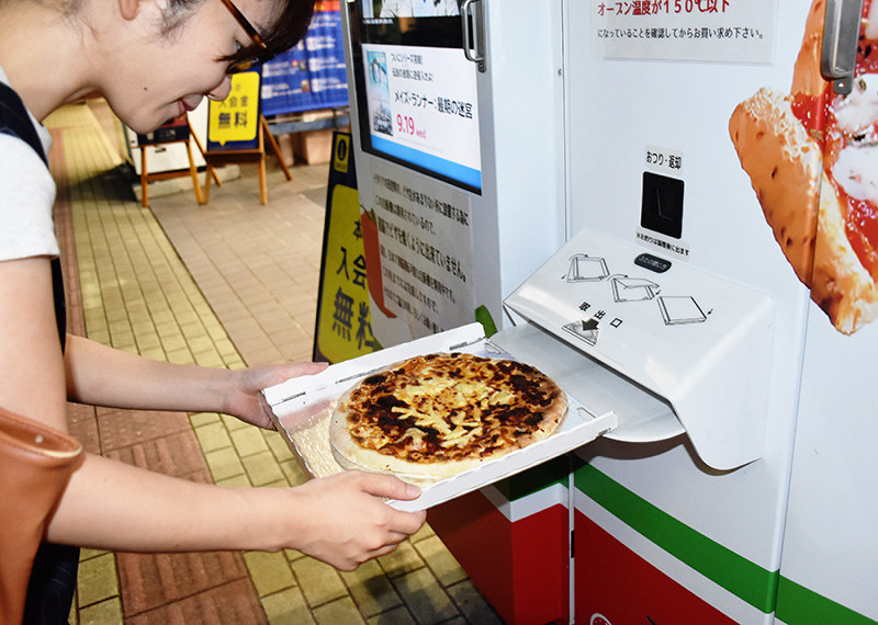 自動販売機から出たきた焼きたてのピザを手に取る買い物客=広島市西区で、隈元悠太撮影