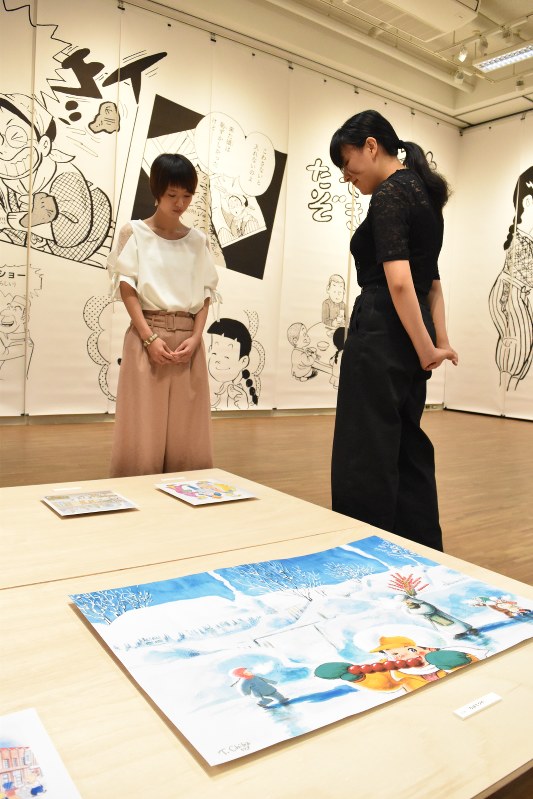 「ヘイセイ」展の作品に見入る学生。手前はちばてつやさんが中国の伝統的な菓子売りを描いた「糖葫蘆(タンフールー)売り」=京都市左京区の京都造形芸術大で2018年9月24日、菅沼舞撮影