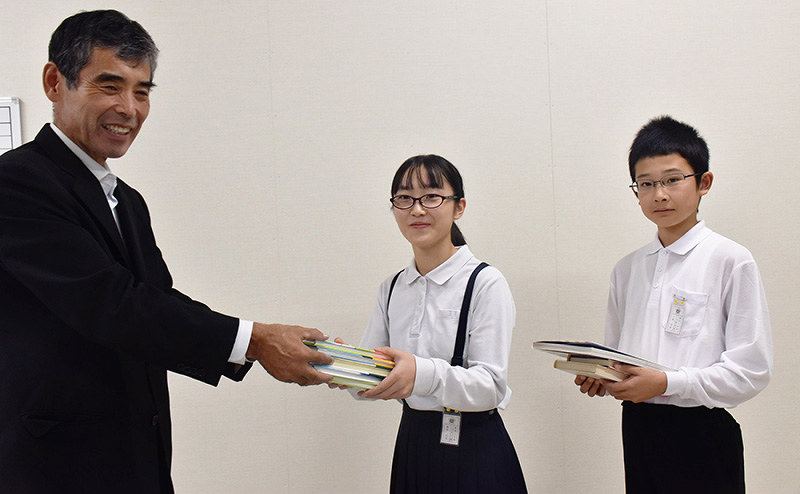 名和川寿夫さん(左)から本を受け取る箭田小の藤原日菜さん(中央)と川崎悠聖さん=岡山県倉敷市真備町上仁万で、戸田紗友莉撮影