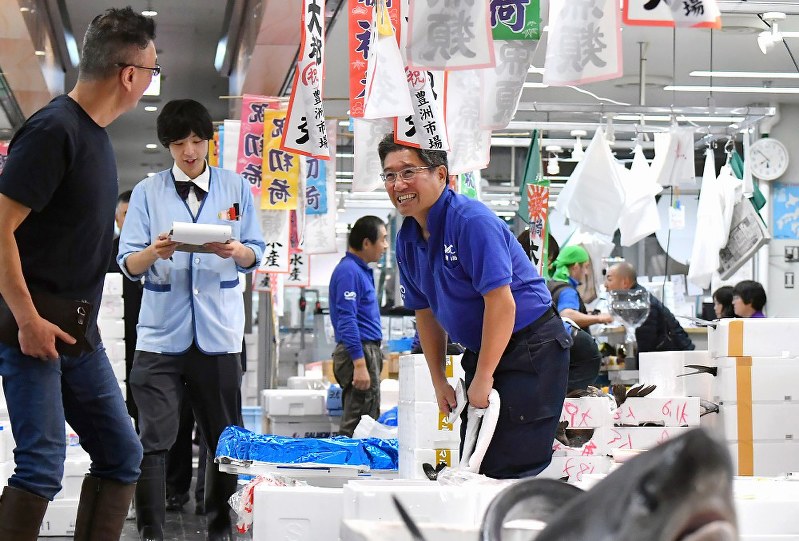 豊洲市場の水産仲卸売場で、顧客の男性に笑顔で頭を下げる「山治」の山崎康弘社長(中央)=東京都江東区で2018年10月11日午前7時51分、竹内紀臣撮影