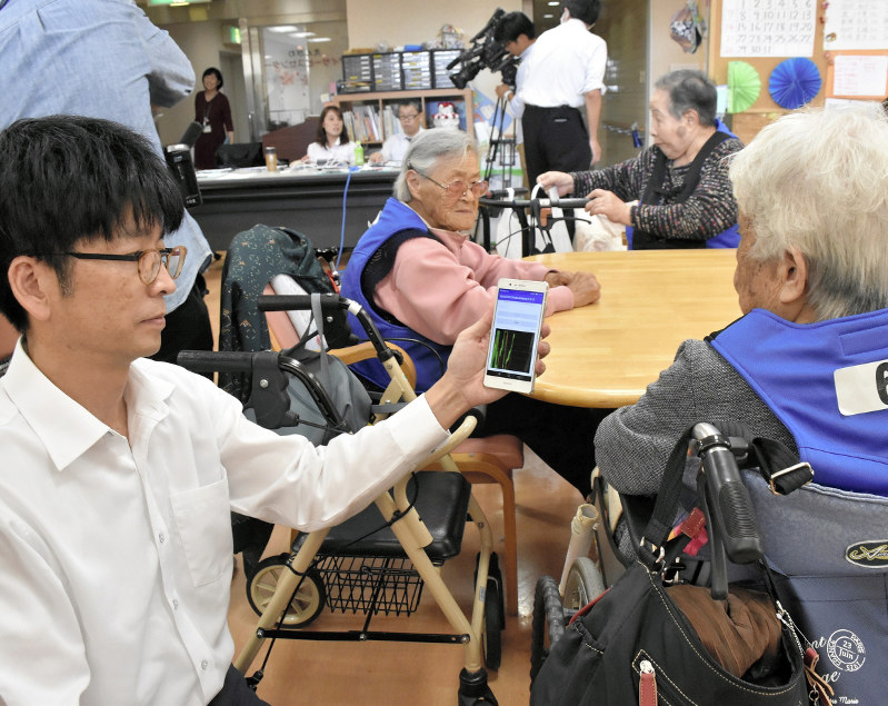 青いベストを着用した利用者から、心拍数などのデータを収集する推進協議会の関係者=高松市鶴市町で2018年10月15日午後1時16分、山口桂子撮影