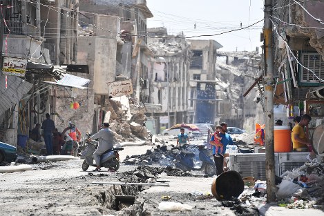 激戦地となり、多くの建物が破壊されたモスル旧市街。かろうじて原形をとどめた建物の１階で小さな飲食店が営まれ、子どもを抱いた男性らが談笑していた。街は至る所にがれきが散乱し、車やバイクが通るたびに粉じんが舞った＝イラク・モスル旧市街で