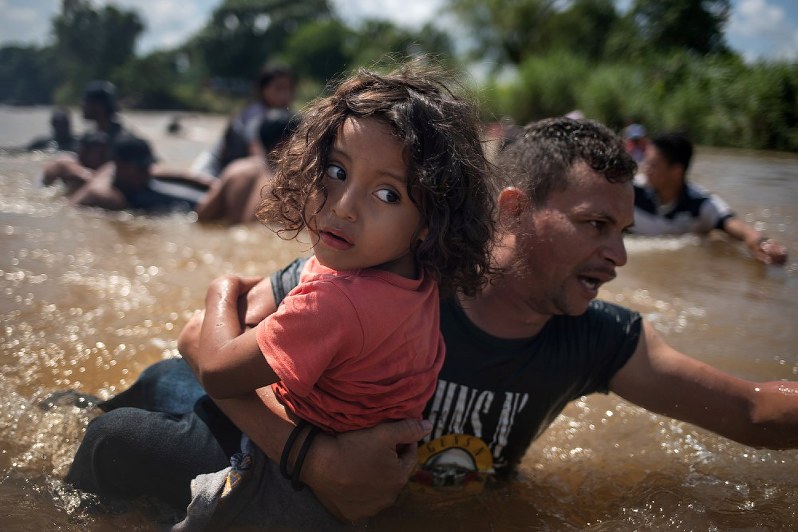 米国を目指す移民の男性に抱えられ、グアテマラとメキシコ国境のスチアテ川を越える少女=29日、ロイター