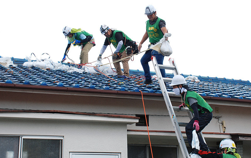 瓦屋根に張ったブルーシートが台風で飛び、土のうを下ろして、再度ブルーシートを張る作業をするボランティア=大阪府茨木市で2018年10月17日、御園生枝里撮影