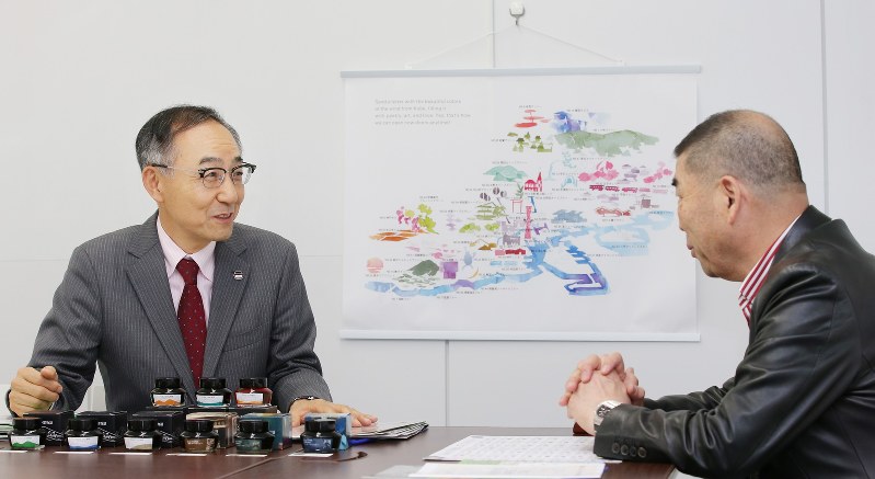 「Kobe INK物語」開発秘話を語るナガサワ文具センターの竹内直行さん(左)と落語家の桂南光さん。後ろの壁にかかる絵は、それぞれの色を使って描かれた神戸の街=神戸市中央区で2018年10月30日、梅田麻衣子撮影