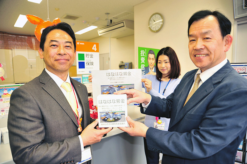 福知山内記郵便局の蒲善光局長(左)に募金箱を託す京都府福知山市市民憲章推進協議会の田村卓巳会長=同市で、佐藤孝治撮影