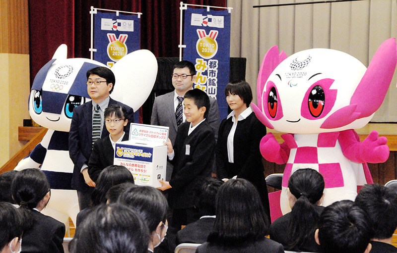 東京2020マスコットのミライトワ、ソメイテイやパラリンピック銅メダリスト広瀬順子さん(右から2人目)らに囲まれ、回収箱を受け取る児童代表=愛媛県新居浜市の市立角野小で、近藤隆志撮影