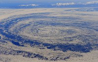沖で渦巻く流氷。後方左端は知床岬＝北海道・オホーツク海で２０１８年２月２日午後１時５６分、本社機「希望」から宮本明登撮影