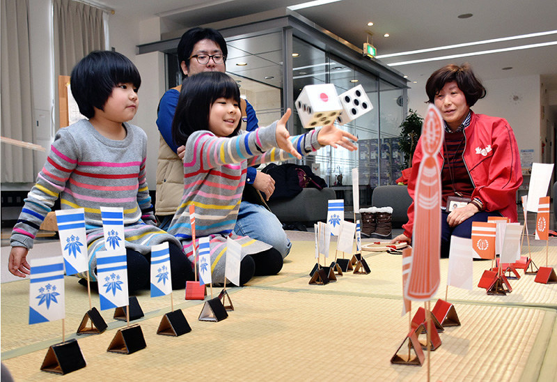 相手の旗を取ろうと笑顔でサイコロを振る女の子(中央)=鳥取市西町3のわらべ館で、園部仁史撮影