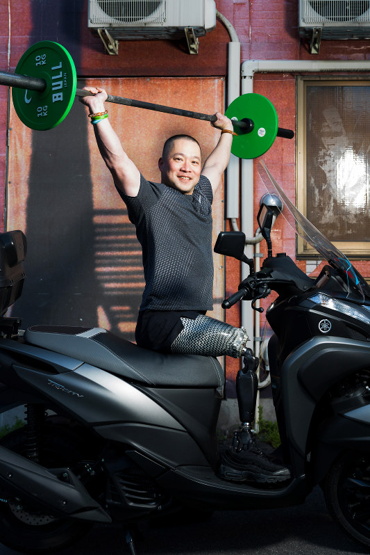大好きなバイクにまたがり、バーベルを挙げる樋口健太郎。競技はあおむけの姿勢で行う=写真家・越智貴雄さん撮影