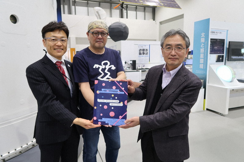 小惑星着陸に挑む探査機はやぶさ2への応援メッセージを吉川真ミッションマネジャー(右)へ贈呈する日本惑星協会の井本昭・事務長。左端は星野好紀・大正製薬ブランドコミュニケーション部長=相模原市中央区の宇宙航空研究開発機構で2019年2月14日、永山悦子撮影