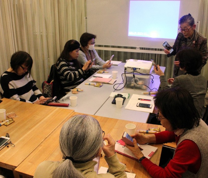 女性講師(右上)が、画面を確認しながら、写真を加工して保存する方法を丁寧に教えていた=東京都世田谷区で