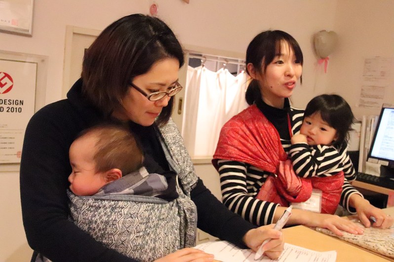 スリングで赤ちゃんを抱っこし、店頭に立つ子連れ出勤のスタッフら=東京都渋谷区のモーハウス青山ショップで