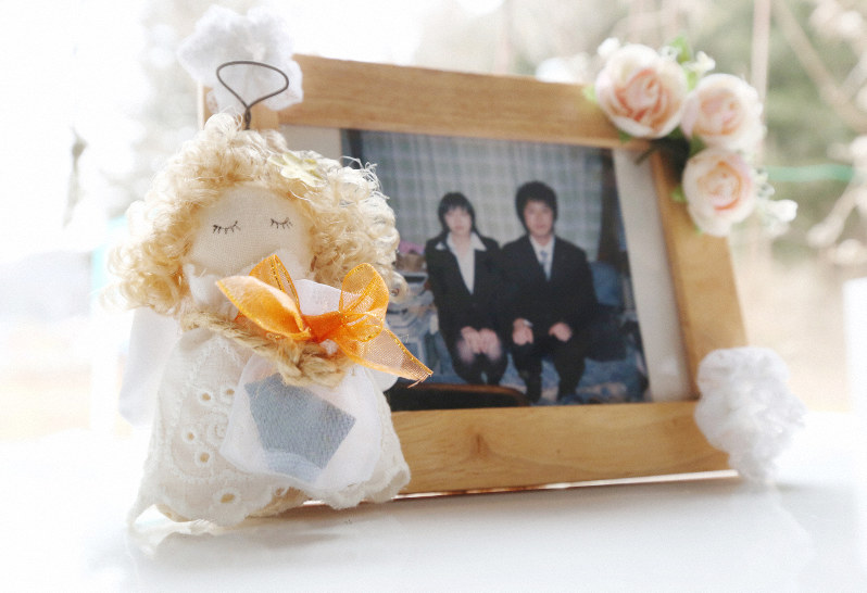 戸羽究さん(右)と妹の杏さんの写真に添えられた天使の人形が、市民会館のタイルが入った袋を抱いていた=岩手県陸前高田市で2019年2月19日、小川昌宏撮影