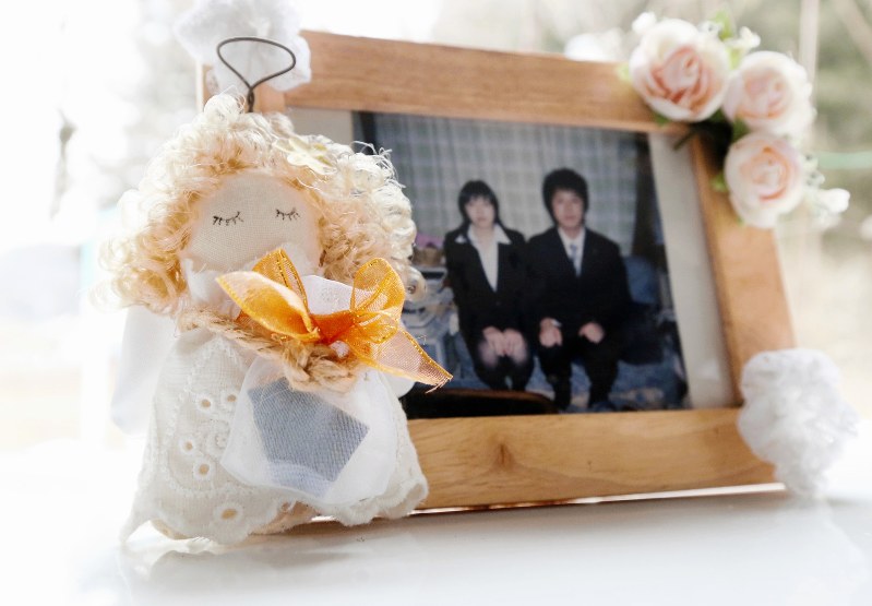 戸羽究さん(右)と妹の杏さんの写真に添えられた天使の人形が、市民会館のタイルが入った袋を抱いていた=岩手県陸前高田市で2019年2月19日、小川昌宏撮影