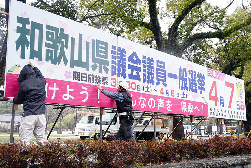 投票を呼びかける啓発看板を設置する作業員=和歌山市一番丁の和歌山城西の丸広場で、木原真希撮影