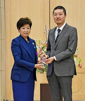 贈呈式で記念品を手にする佐藤准教授(右)と小池知事