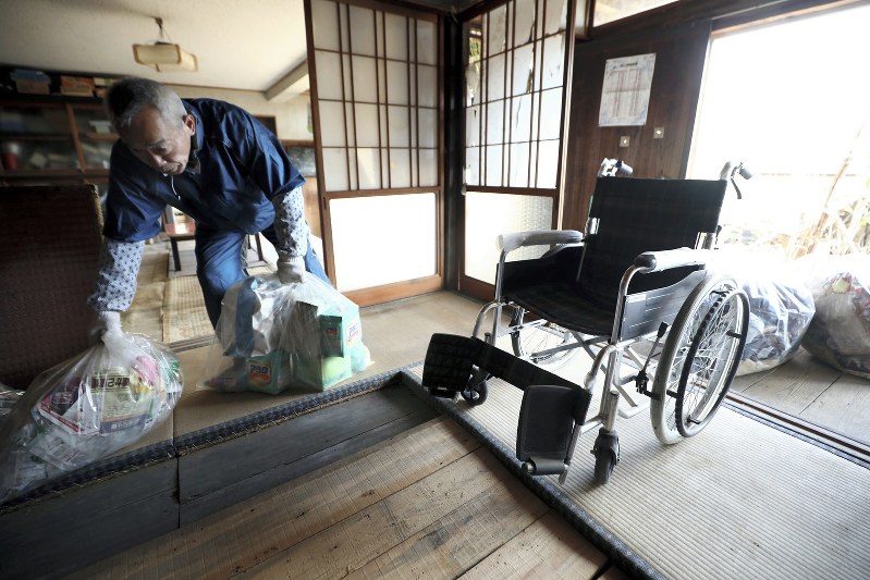 解体に備え、母トミノさん(享年89)の車いすが残された自宅を片付ける居村久男さん(66)。トミノさんは2年前、新潟県の避難先で亡くなった。父丒治さん(92)は神奈川県に避難し古里に戻る見通しは立っていないが、今も自宅の解体を拒んでいるという=福島県浪江町で2019年2月1日、喜屋武真之介撮影
