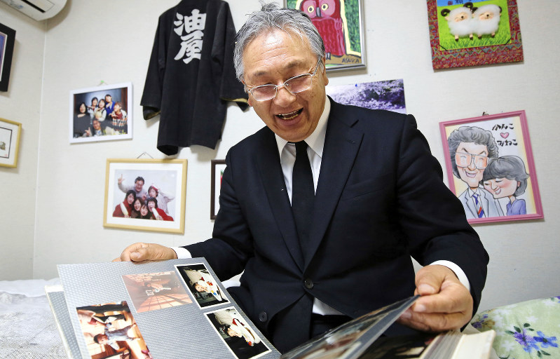 生活する仮設住宅で、家族のアルバムを見つめて笑顔を見せる佐々木一義さん。壁には家族写真が飾られていた=岩手県陸前高田市で2019年3月10日、小川昌宏撮影
