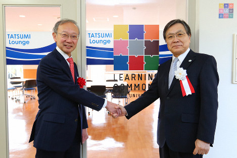 「タツミ　ラウンジ」前で握手する武田広・神戸大学長（右）と橋本一孝常務