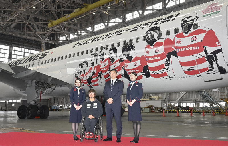 特別塗装された機体の前で記念撮影する五郎丸歩選手(中央右)と池崎大輔選手(同左)=羽田空港で2019年3月19日午前10時40分、藤井達也撮影