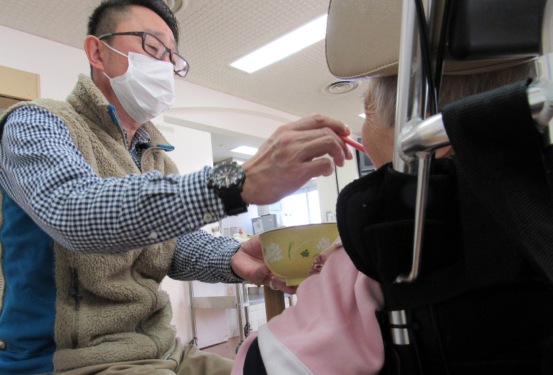 昼食をとる和美さん(右)。職員の介助が絶えず必要だ=群馬県高崎市で