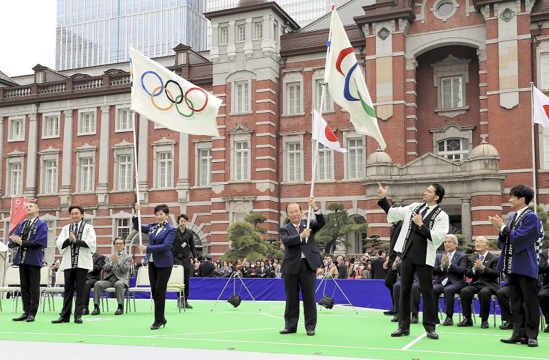 TOKIOから受け取った五輪旗、パラリンピック旗を掲げる東京都の小池百合子知事(中央左)と東京五輪・パラリンピック組織委の武藤敏郎事務総長(同右)=東京都千代田区の東京駅丸の内中央広場で2019年3月30日、梅村直承撮影
