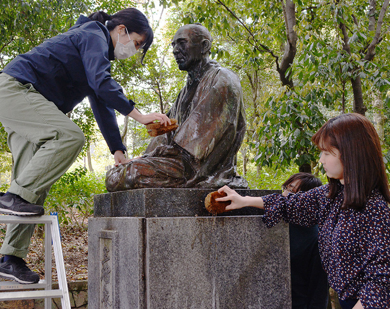 玉楮象谷の像をたわしで磨く研究生たち=高松市番町の市立中央公園で、金志尚撮影