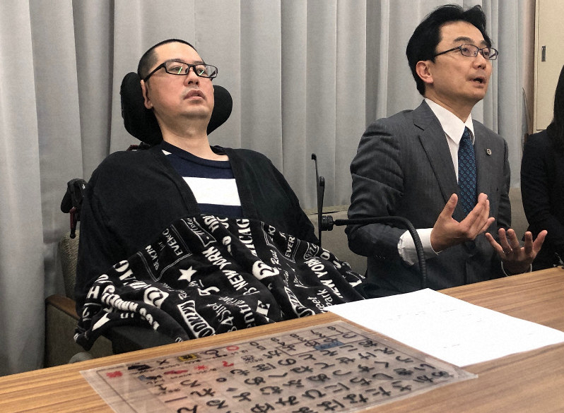 50音が書かれた文字盤を前に記者会見する高田泰洋さん(左)と支援する藤岡毅弁護士=さいたま市浦和区の埼玉県庁で2019年4月16日午後1時48分、畠山嵩撮影